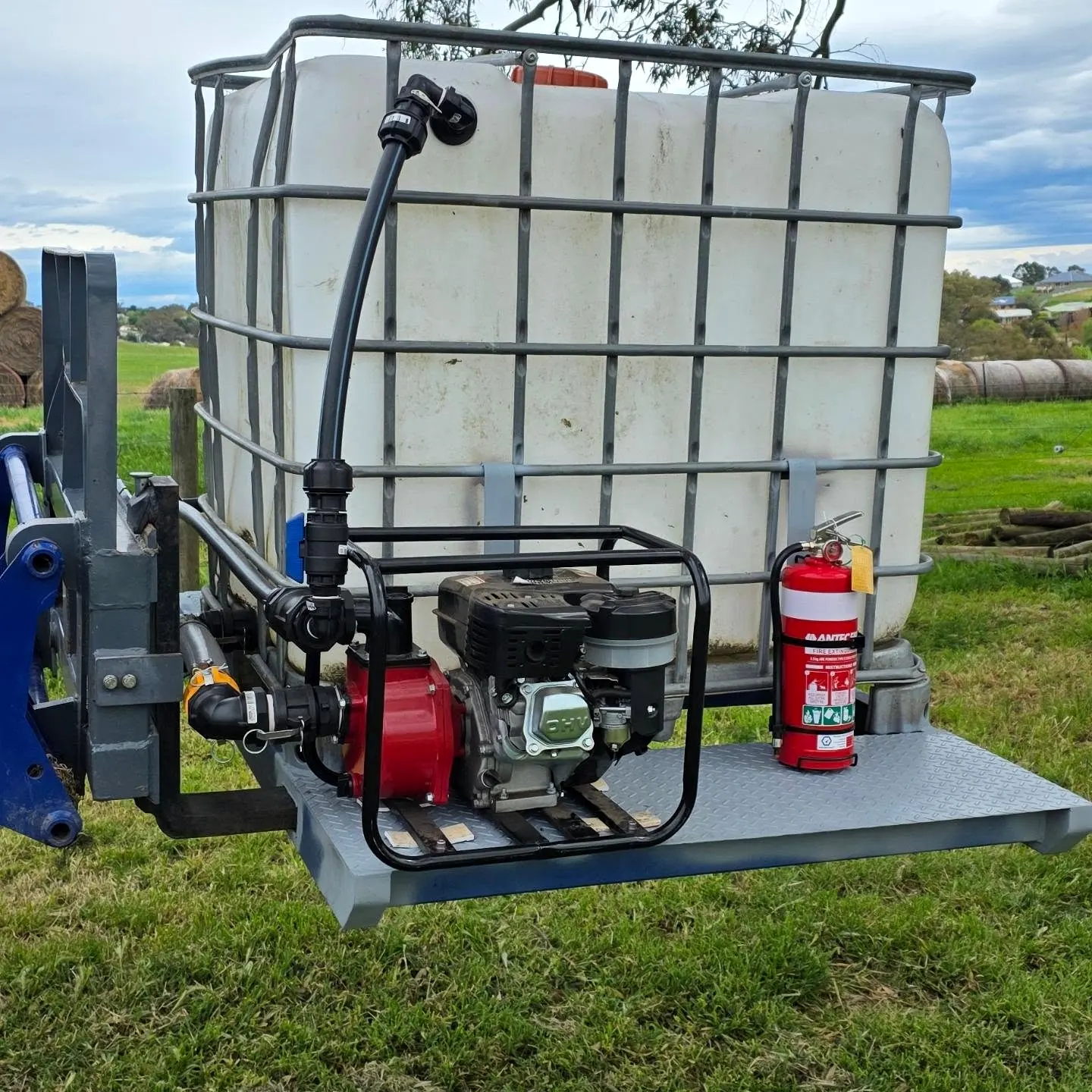Farm firefighting skid unit on tractor forks: water tank, red fire pump, hose and extinguisher on a steel skid