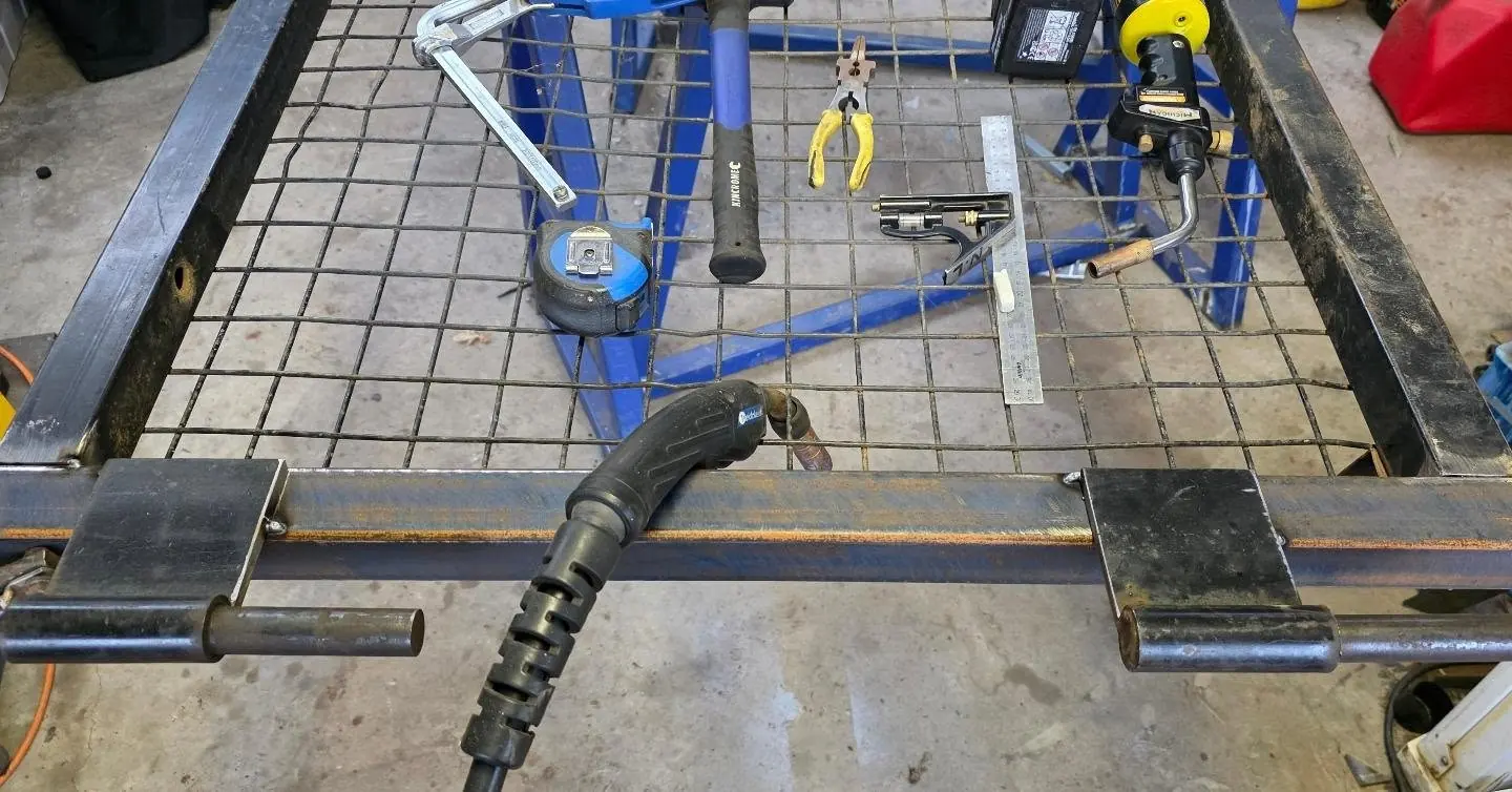 Trailer cage gate on blue trestles with a new upright, welding torch and tools